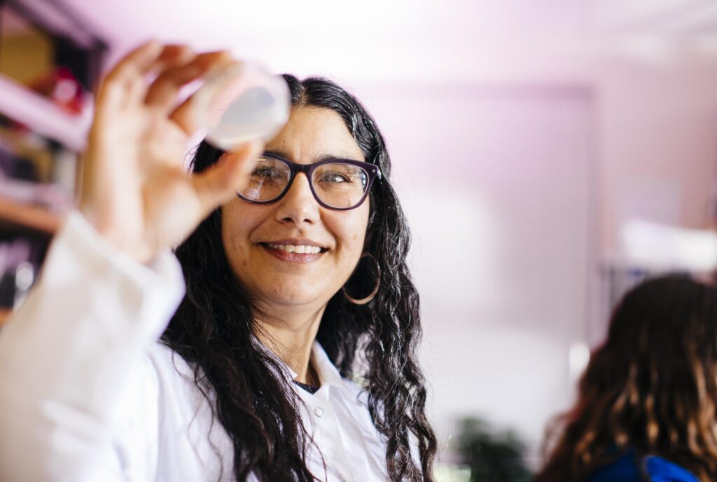 Researcher holding up a sample in a petri dish and smiling.