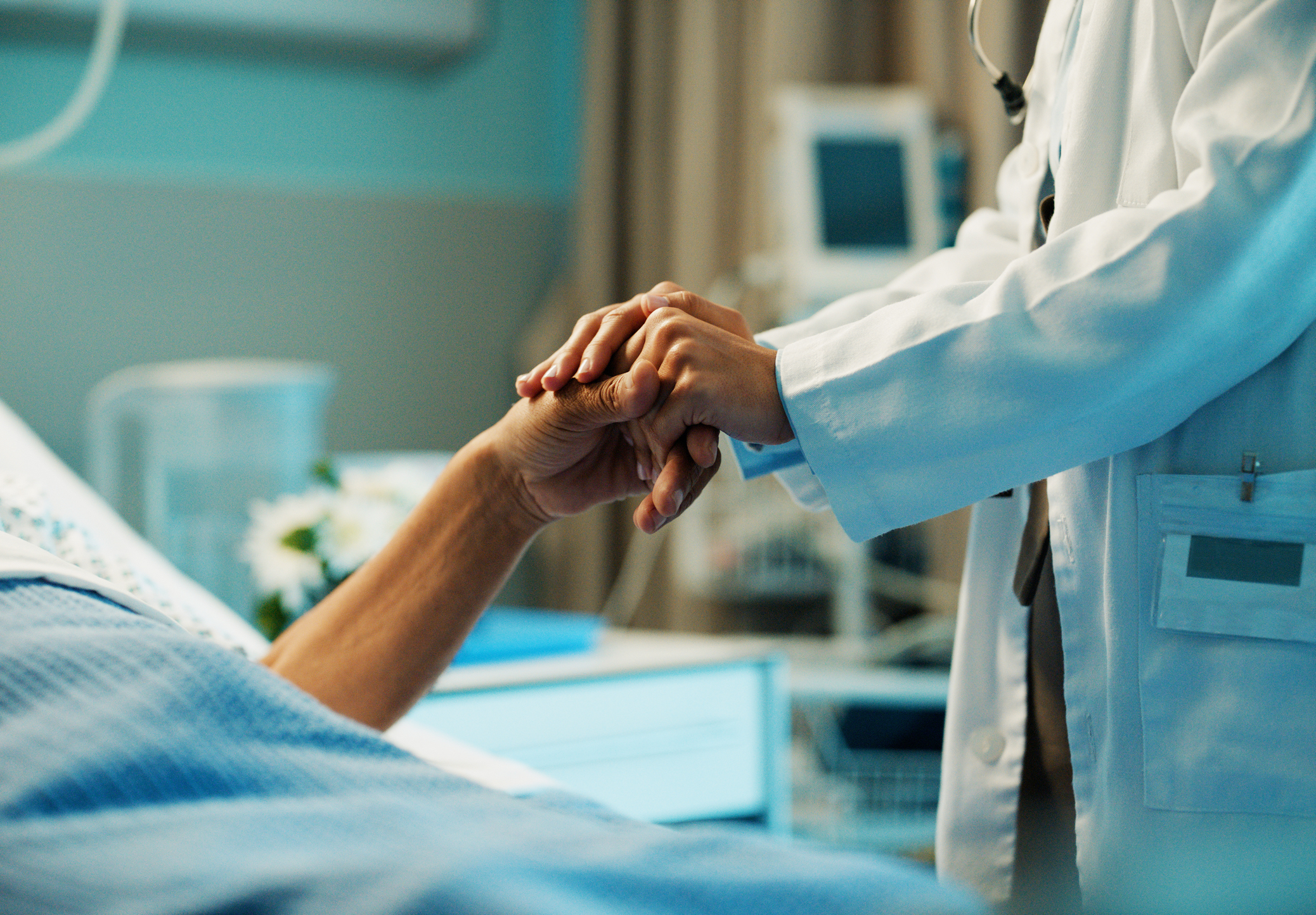 Doctor holding the hand of a patient who is clearly in the hospital.